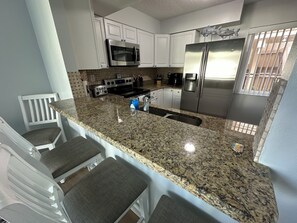 A kitchen with white cabinets, a stainless steel refrigerator, a microwave, and a granite countertop. - Waterfront 2 bed/2 bath condo on Boca Ciega Bay on highly desirable Isla del Sol (St. Petersburg)