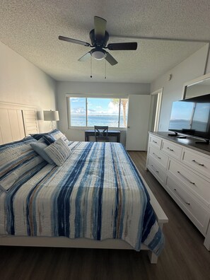 A bedroom with a bed, a desk, a television, and a window with a view of the water. - Waterfront 2 bed/2 bath condo on Boca Ciega Bay on highly desirable Isla del Sol (St. Petersburg)