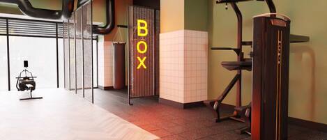 Un gimnasio moderno con equipo de ejercicio, una amplia mesa de madera y una pared con la palabra "BOX" en letras llamativas.