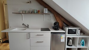 Cocina compacta con lavamanos, lavavajillas, microondas y una repisa con varios objetos.