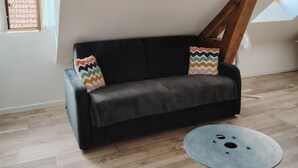 Una habitación con un sofá de cuero negro, una mesa redonda de metal, suelo de madera y un techo inclinado con tragaluz.