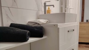 Un baño moderno con salpicadero de mármol blanco, un lavabo con grifo, un espejo y un cubo de basura.