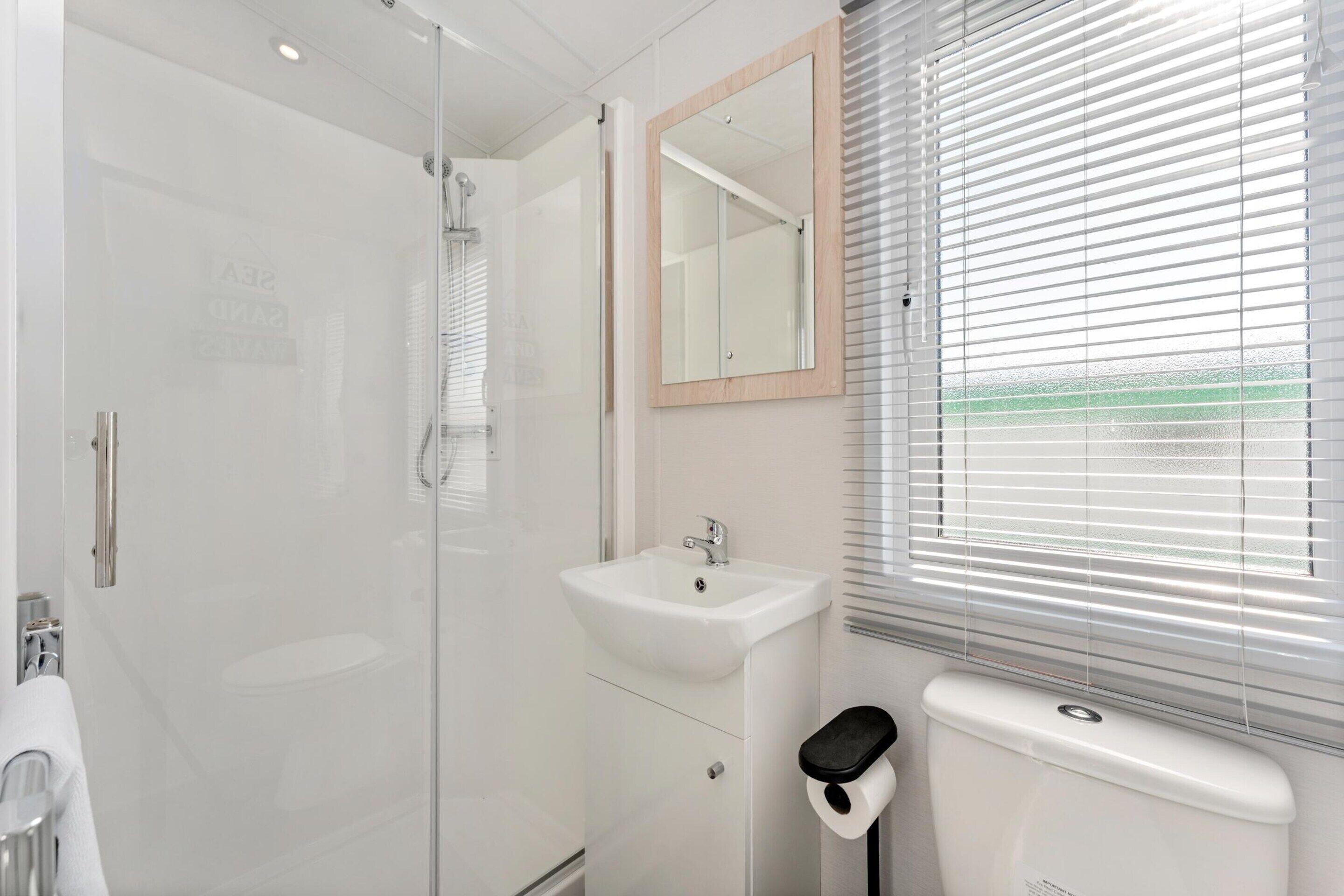 A modern bathroom with a glass-enclosed shower, a white sink, and a toilet.