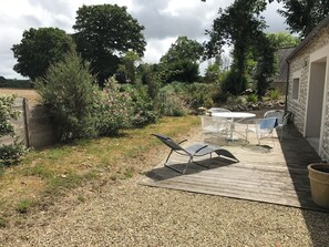 Un patio con una mesa y sillas, rodeado por un jardín con diversas plantas y árboles.