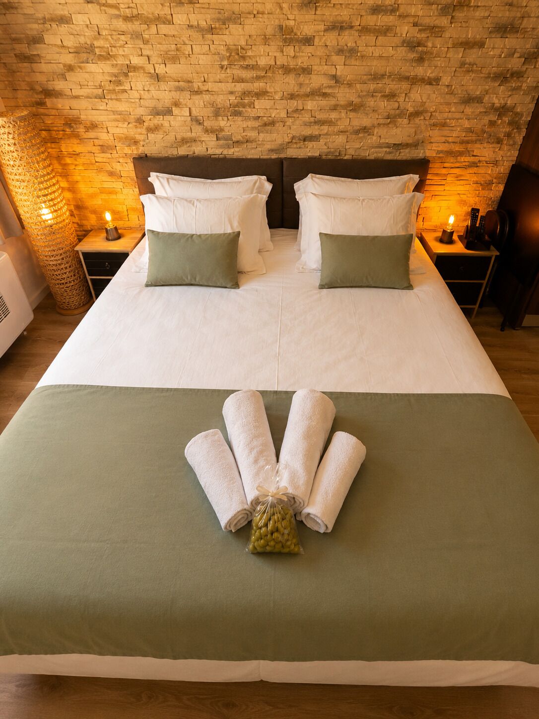 Un lit double avec une literie blanche et verte, une petite table de chevet avec une lampe, et un mur avec un motif en briques.