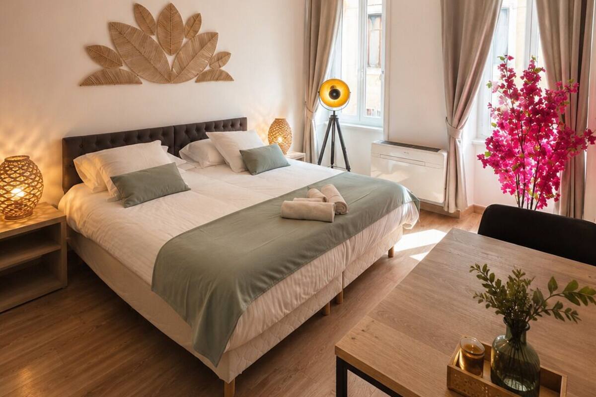 A well-lit room with a bed, bedside lamps, a table with a vase, and a window with curtains.