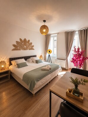 A well-lit room with a bed, bedside lamps, a table with a vase, and a window with curtains.