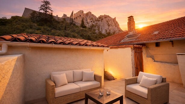 A patio with two wicker sofas and a coffee table, overlooking a mountainous landscape at sunset. - Le Clos Androne (Sisteron)