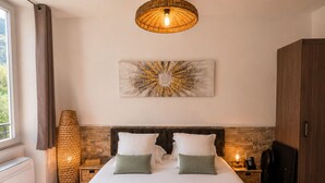 A hotel room with a bed, a large woven light fixture, a wall-mounted artwork, and a wooden wardrobe. - Le Clos Androne (Sisteron)
