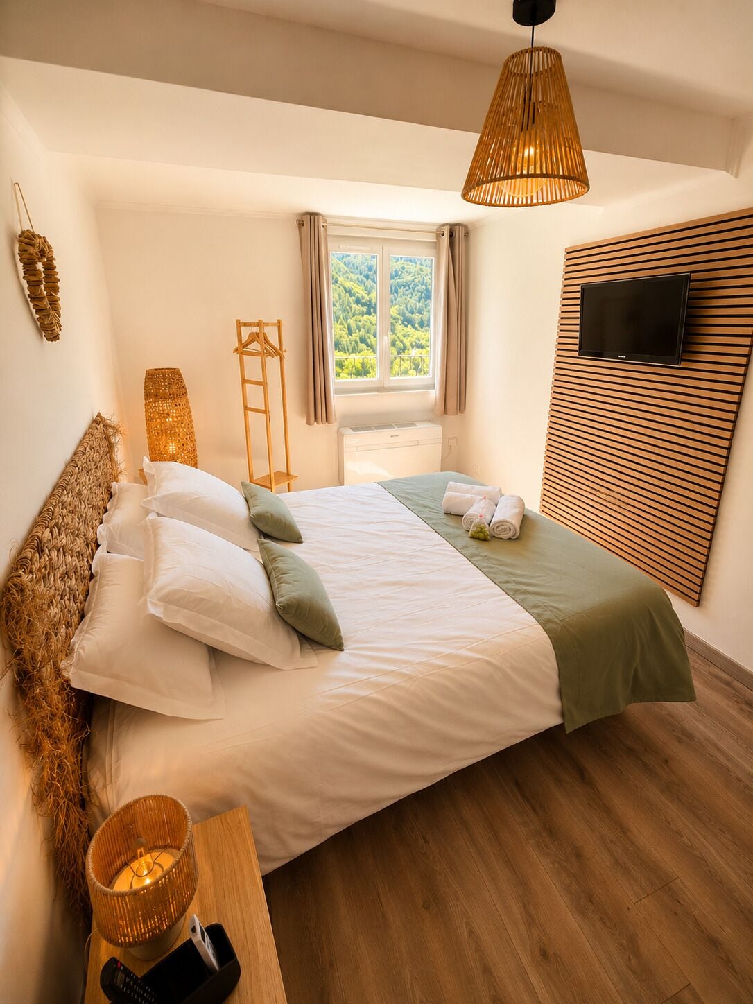 Un dormitorio con una cama, un televisor, una ventana con cortinas y piso de madera.