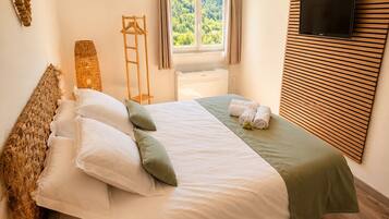 Un dormitorio con una cama, un televisor, una ventana con cortinas y piso de madera.