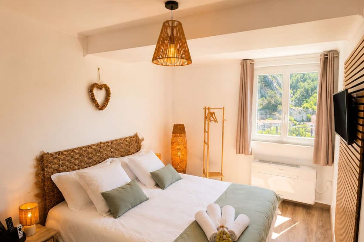 A neatly made bed with a green throw, a bedside lamp, and a heart-shaped decoration on the wall.
