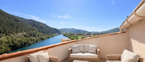 Un balcón con muebles de mimbre y vistas a un río y montañas.