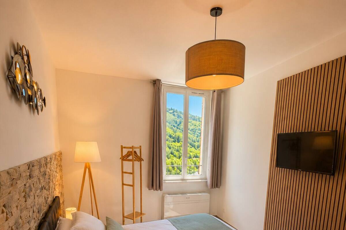 A bedroom with a bed, bedside lamps, a TV, a window with a view, and a wooden wall panel.