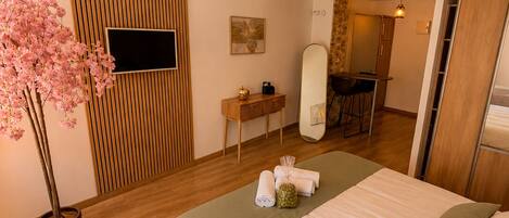 A hotel room with a bed, a wooden wall panel, a TV, a mirror, a small table, and a potted plant.