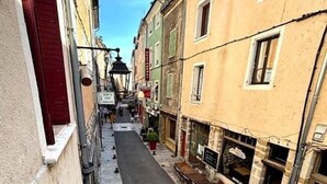 A narrow street with buildings on either side, outdoor seating, and a clear sky. - Le Clos Androne (Sisteron)
