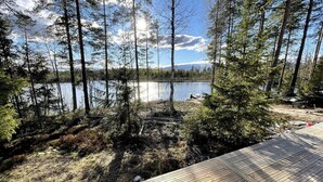 Una terraza de madera con vistas a un lago, árboles y cielo despejado.