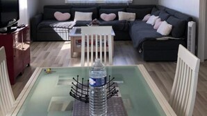 A modern living room with a sofa, a dining table with chairs, a TV, and a window with curtains. - Country house with a change of scenery (Velet)