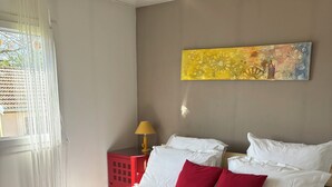 A hotel room with a bed, red and white bedding, a red nightstand with a lamp, and a painting on the wall. - Country house with a change of scenery (Velet)