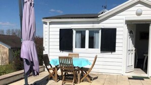 A white mobile home with a patio area, a table with chairs, and a covered bench. - Country house with a change of scenery (Velet)