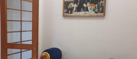 Ein Zimmer mit einer Holztür, einem blauen Sofa mit Goldakzenten und einem Gemälde an der Wand.