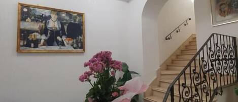A room with a staircase, a painting on the wall, and a desk with papers.