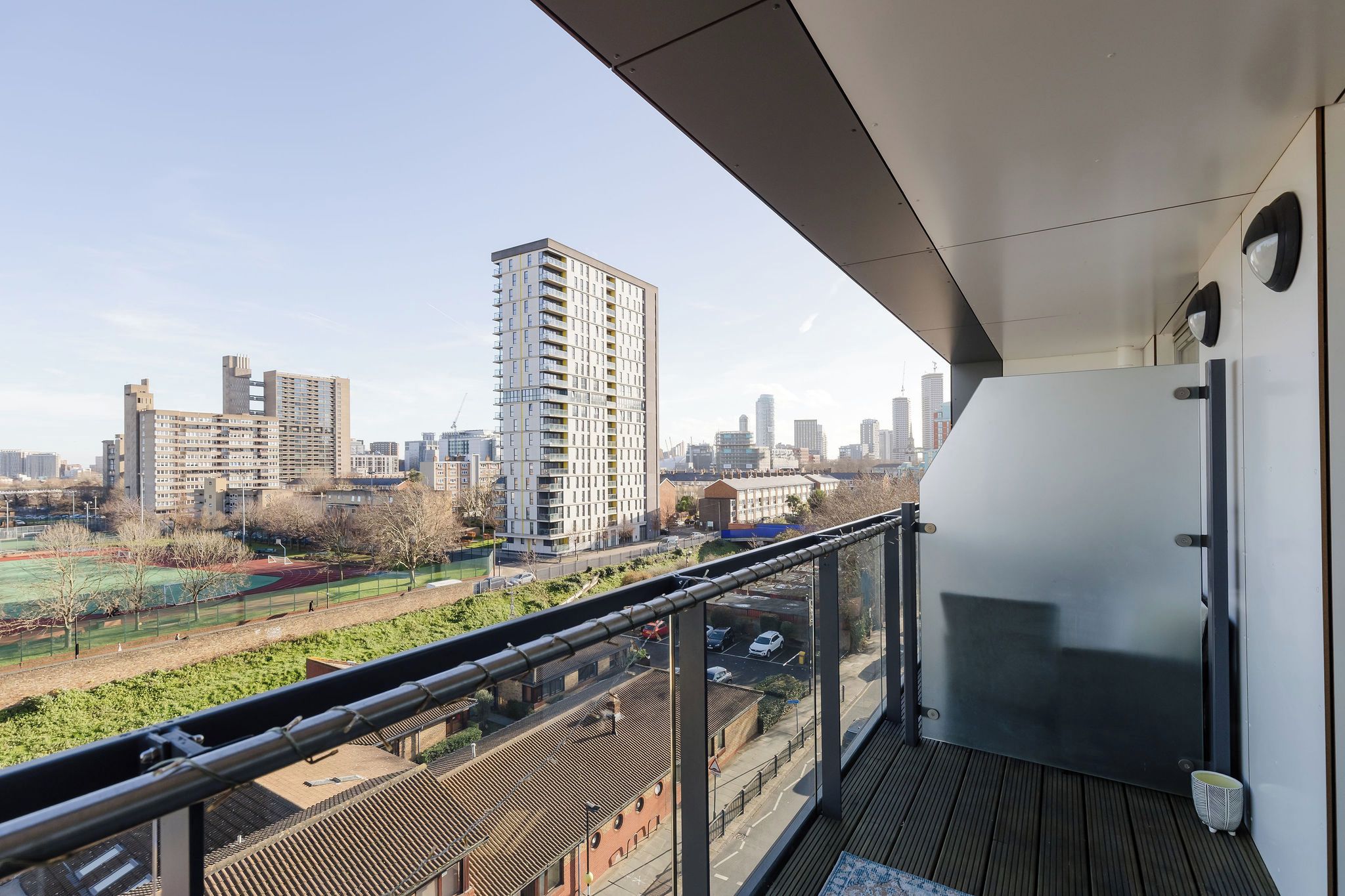 A balcony with a city view, a modern building, and a sports field.