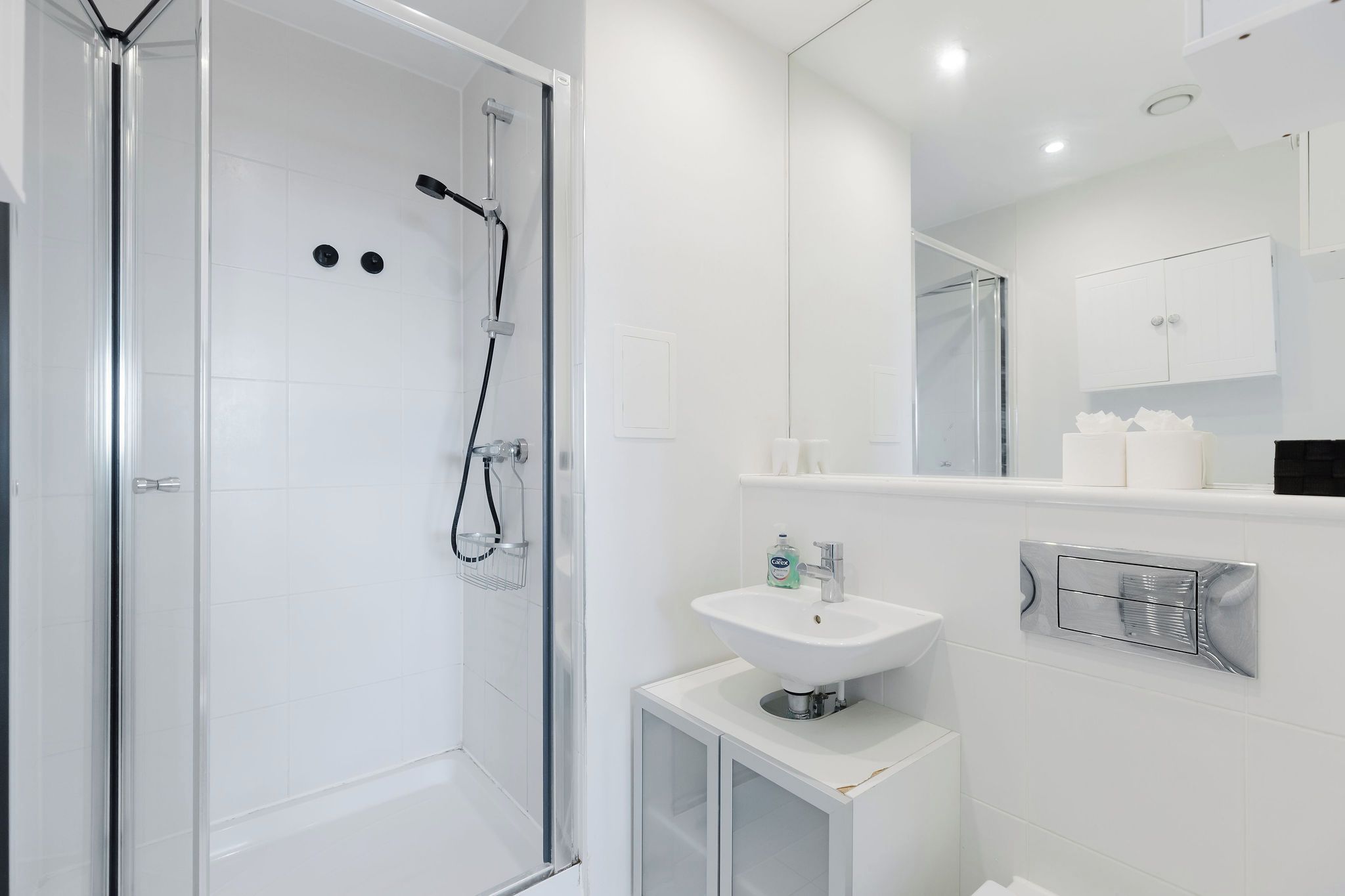 Ein modernes Badezimmer mit einer ein Glasfachwerk-Dusche, einem weißen Waschbecken und einem Spiegel darüber.