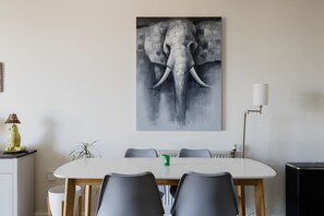 Ein Essbereich mit einem weißen Tisch, grauen Stühlen, einem grünen Kerzenleuchter und einem großen Elefantenbild an der Wand.