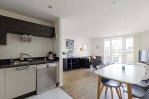 Eine moderne Küche mit Geschirrspüler, einem Esstisch mit Stühlen, einer Couch und einem großen Fenster mit Blick auf die Stadt.