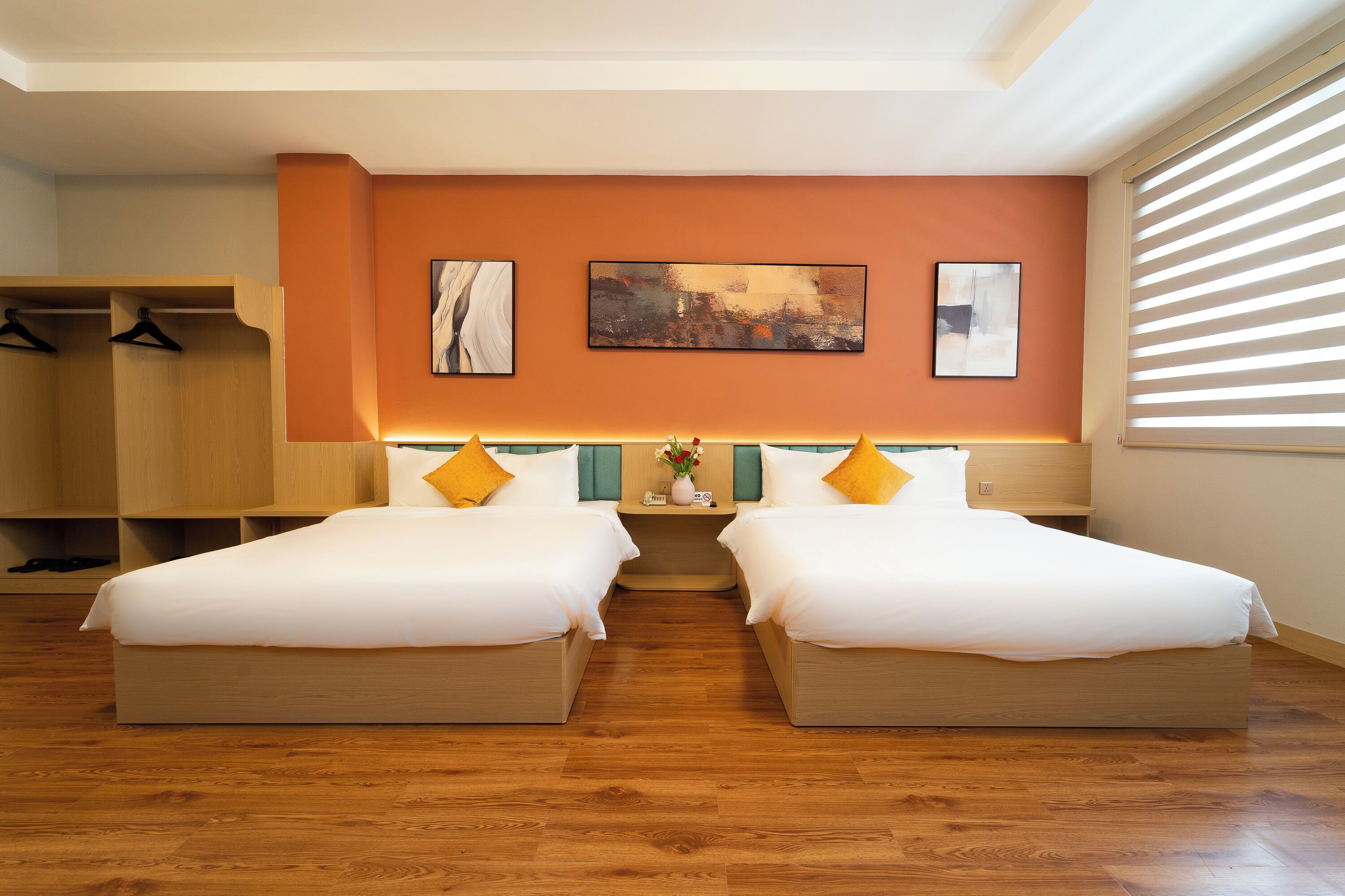 Ein Hotelzimmer mit zwei Betten, Holzboden, einem Kleiderschrank und Bildern an den Wänden.
