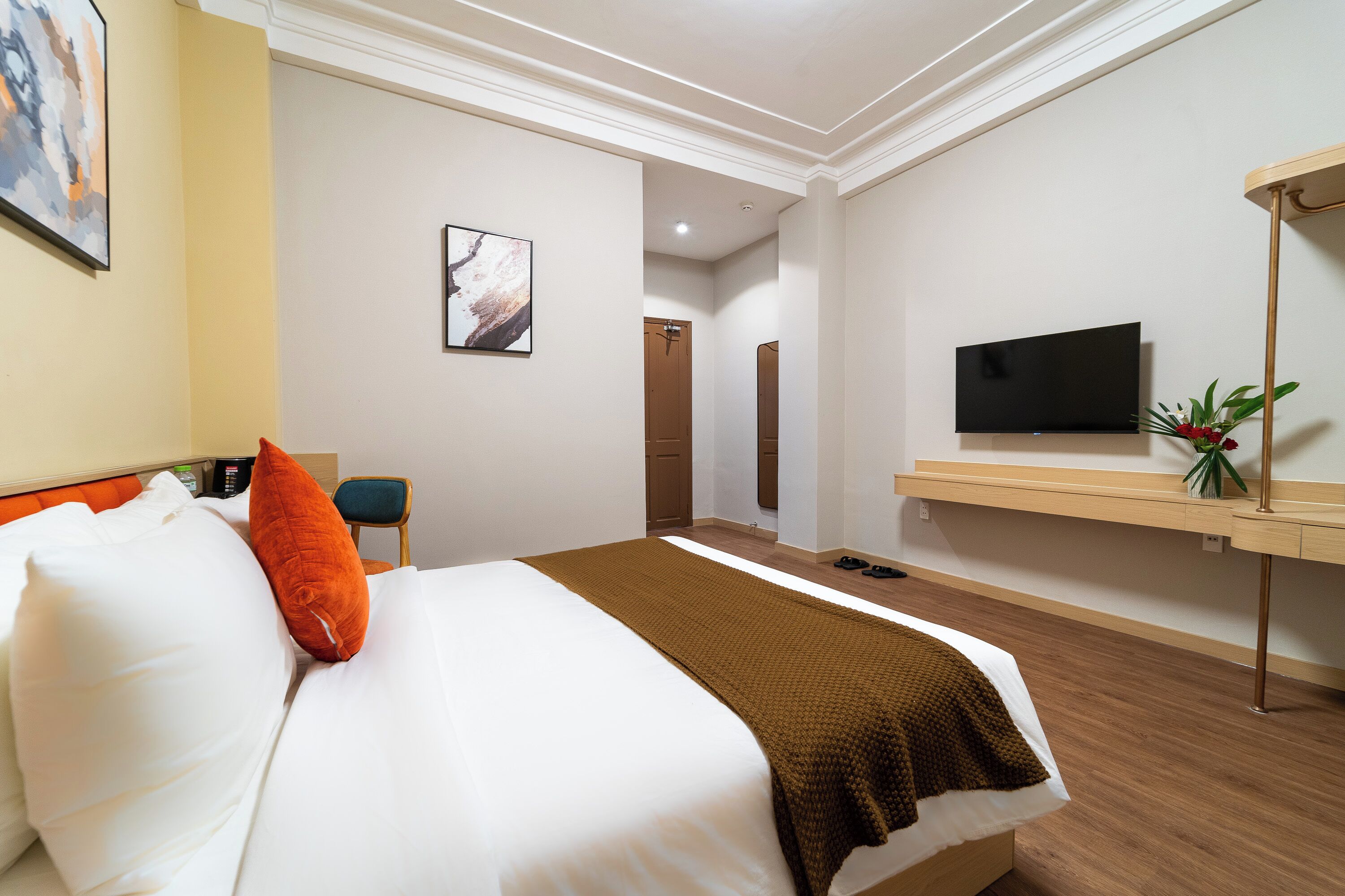 A hotel room with a bed, a TV, a desk, and a plant.