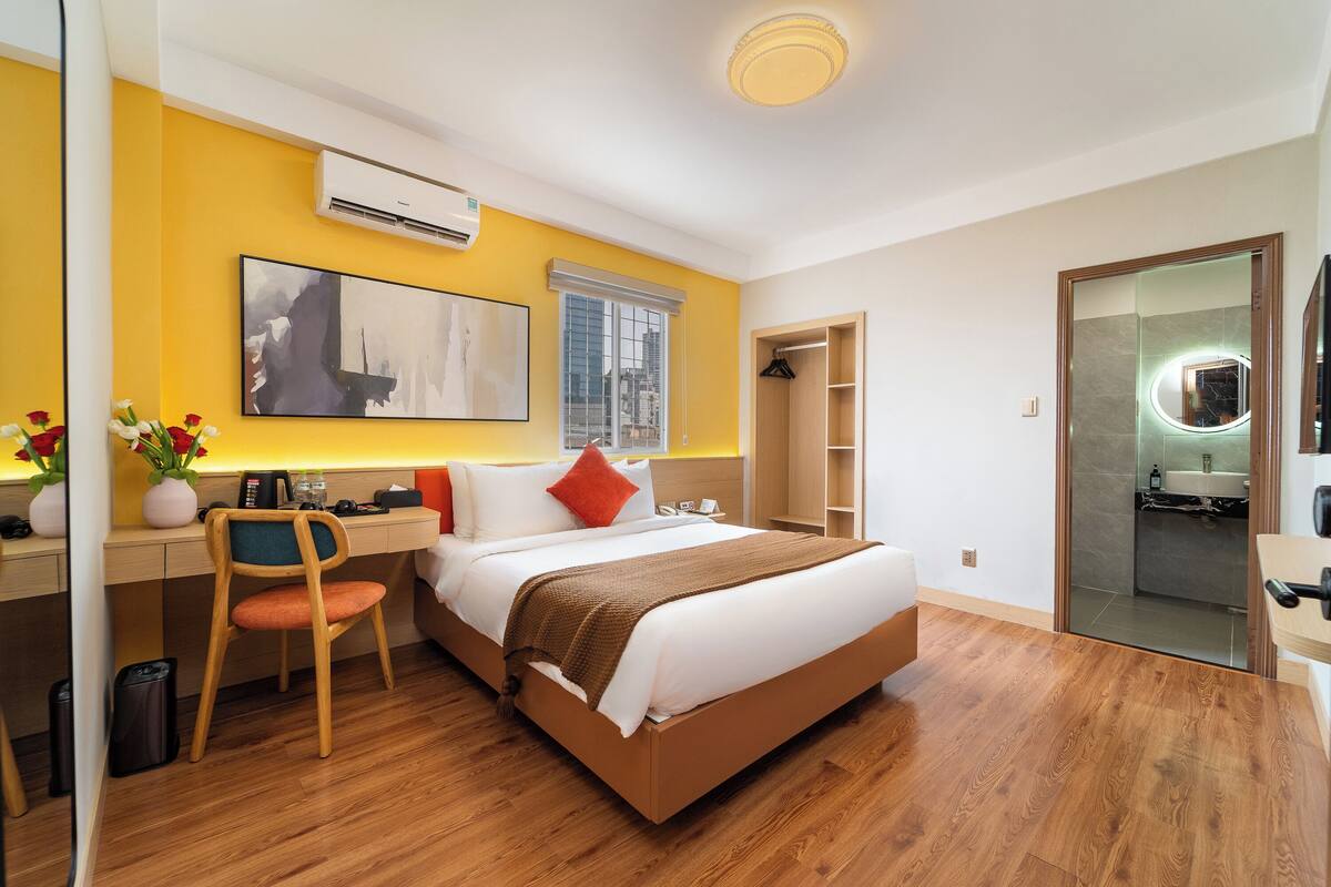 A hotel room with a bed, desk, chair, and a mirror with a light.