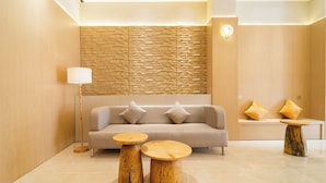 Eine moderne Lobby mit einem beigen Sofa, zwei Holznachttischen und einer Wand mit Steinoptik.