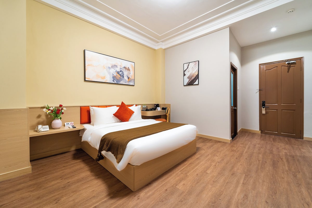 A hotel room with a bed, bedside table, artwork, and a door.