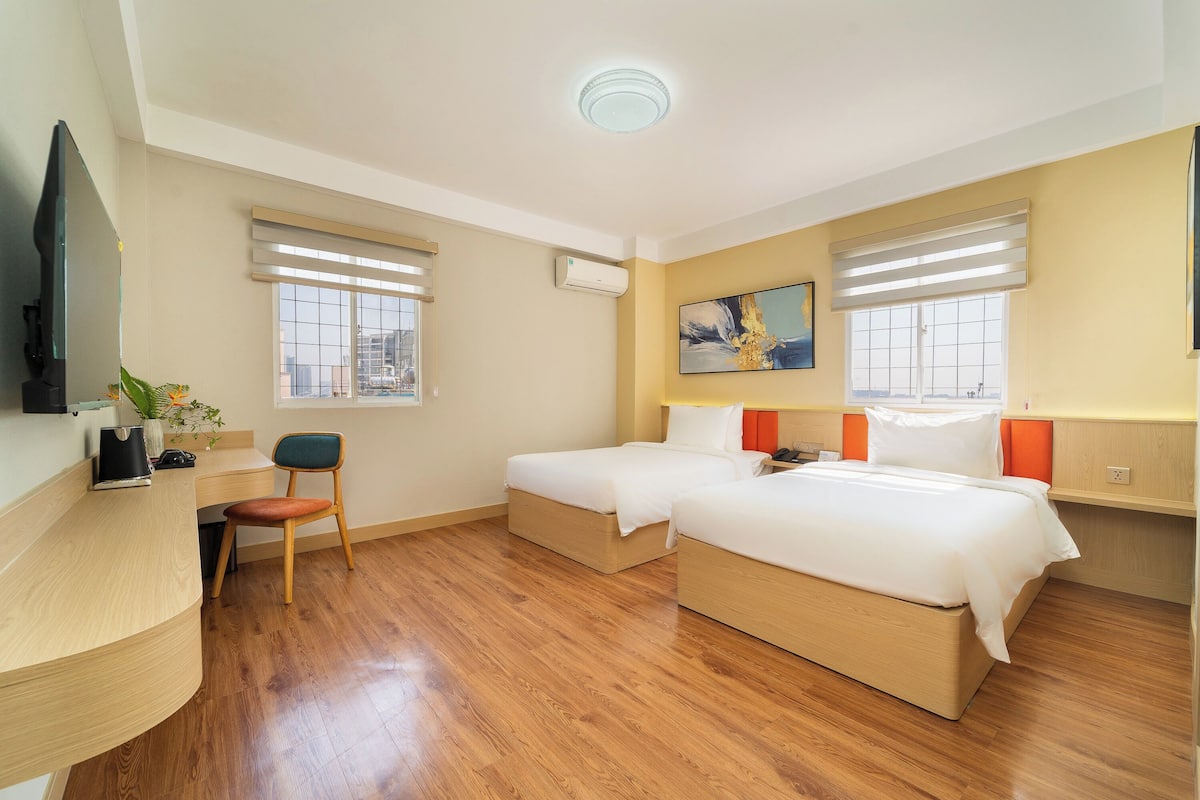 A hotel room with two beds, a desk, a chair, a TV, and a painting on the wall.