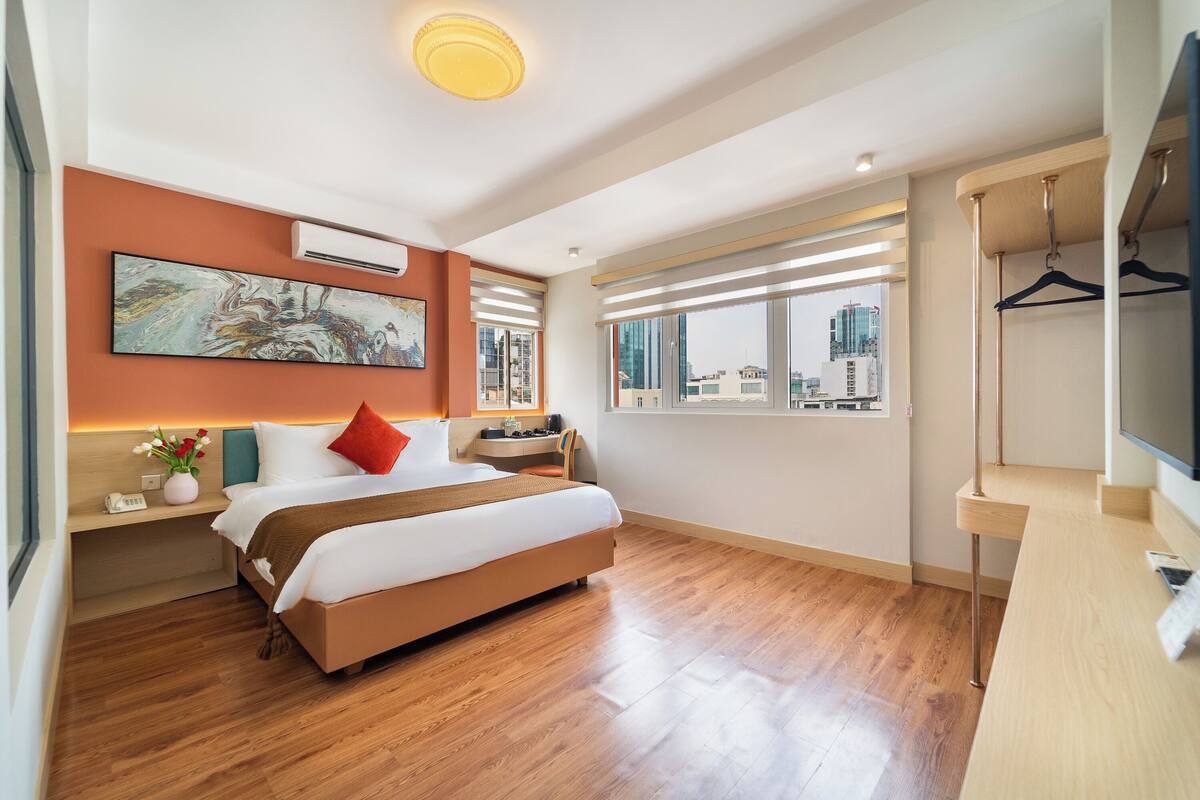 A modern hotel room with a large bed, a desk, a TV, and a city view.
