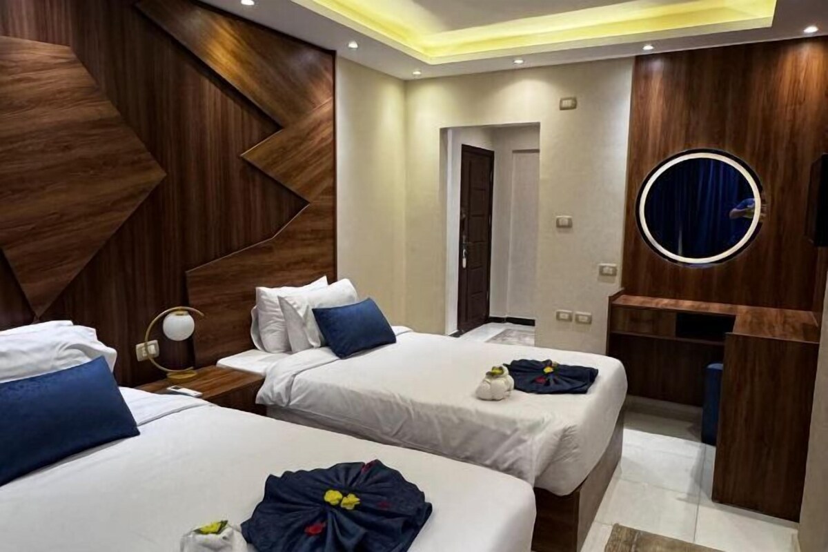 A hotel room with two beds, a round mirror, and a wooden accent wall.