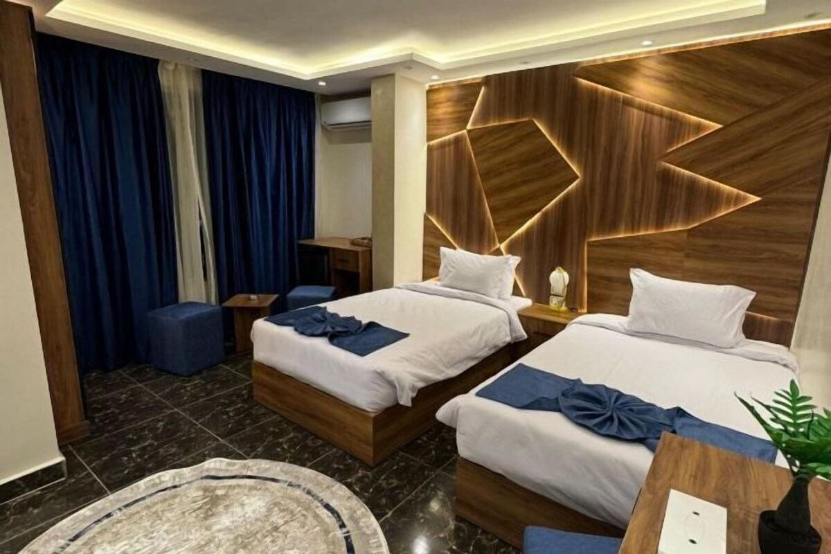 A hotel room with two beds, a desk, a chair, and a large window with curtains.