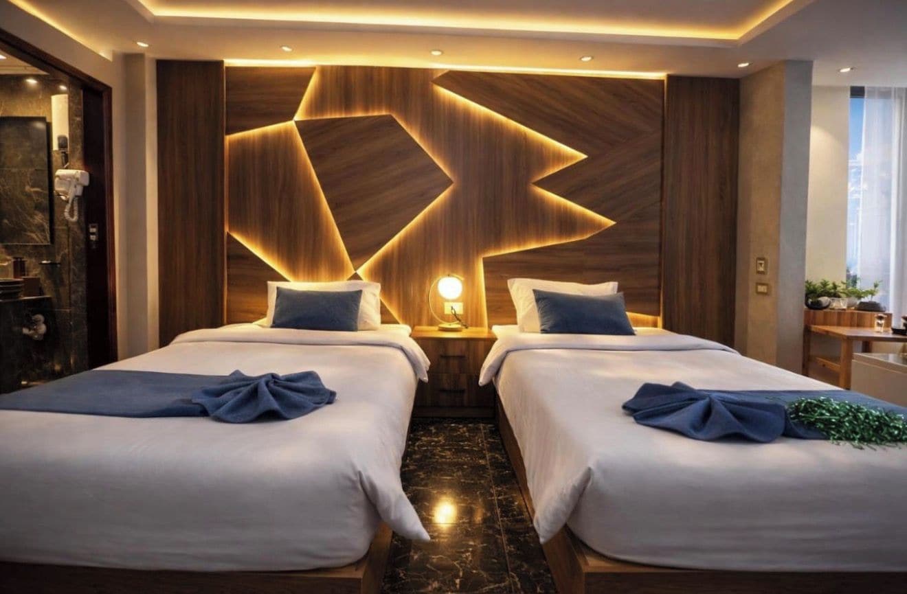 A hotel room with two beds, a wooden accent wall, a marble floor, and a nightstand with a lamp.