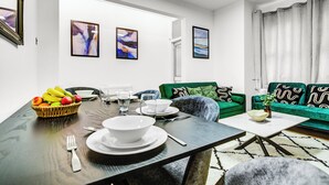 A modern living room with a dining area, featuring a dark wooden table, green sofas, and abstract art on the walls. - Large Semi-detached 4BD 3Bath Long Stay Discount, Wifi, Driveway Parking, Garage (Hounslow)