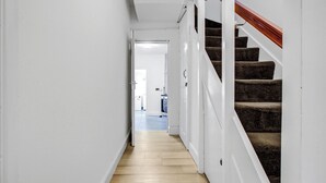 A narrow hallway with a wooden floor leading to a staircase with dark carpeted steps. - Large Semi-detached 4BD 3Bath Long Stay Discount, Wifi, Driveway Parking, Garage (Hounslow)