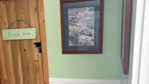 A room with a wooden door labeled "Private Area," a framed picture of a lighthouse, a bed with a patterned pillow, and a white bucket on the floor. - Lake Huron views, ideally located in Eastern UP.Has deck, wildlife, and privacy. (Hessel)