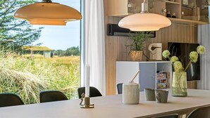 Moderni keittiö, jossa on riippuvalaisimet, ruokapöytä ja näkymä ulos.