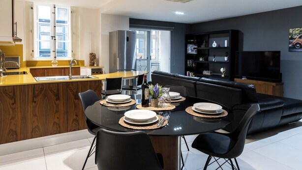 A modern kitchen with a dining area, featuring a central island, black chairs, and a black sofa.