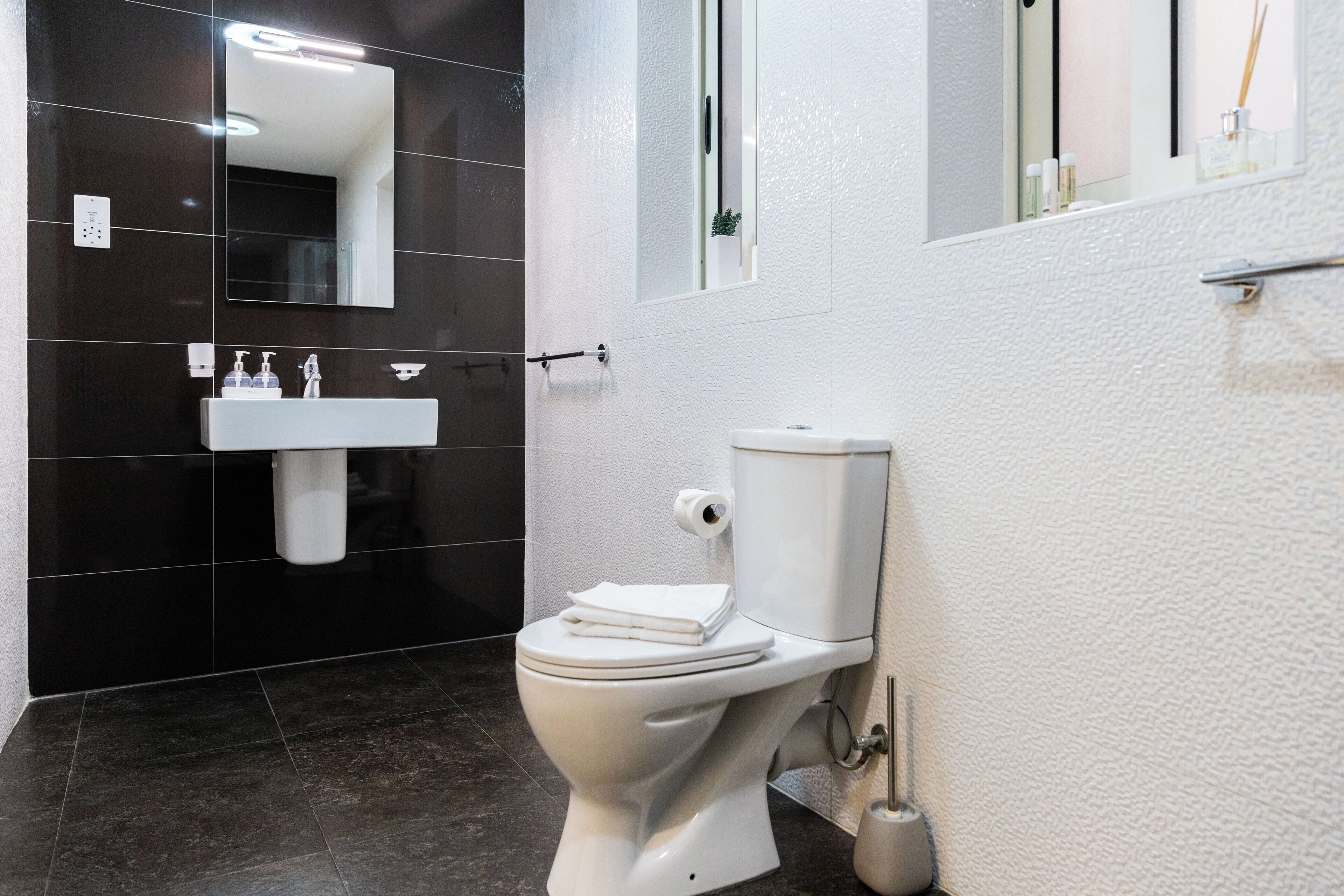 A modern bathroom with a white toilet, a white sink, and a black tiled wall.