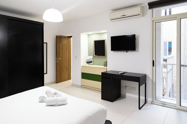 Una habitación de hotel moderna con una cama, un escritorio, una televisión y un ventanal corredera al exterior.