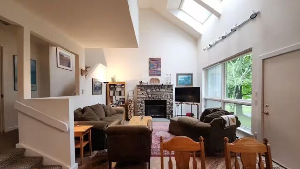 Un salon spacieux doté d’une cheminée en pierre, d’une grande fenêtre et d’un escalier menant à l’étage supérieur.