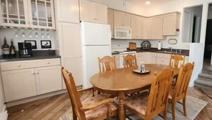 Une cuisine compacte avec des meubles blancs, un îlot central et un coin repas doté de chaises en bois.