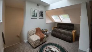 Une pièce avec un plafond en pente, un canapé, un fauteuil et deux tableaux encadrés accrochés au mur.